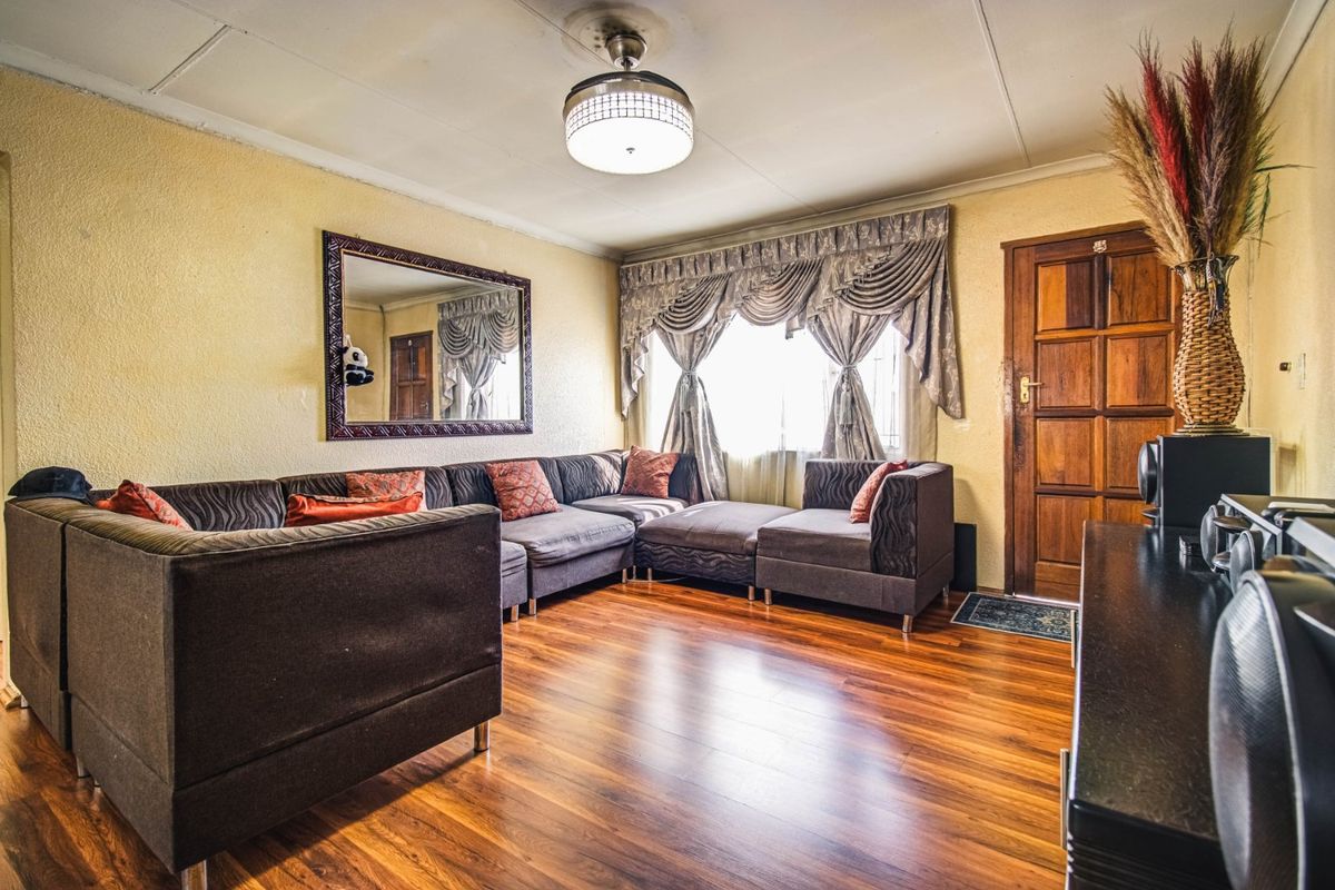 A living room featuring laminate flooring, a ceiling fan, and a solid timber entrance door, with visible wear on the ceiling panels.
