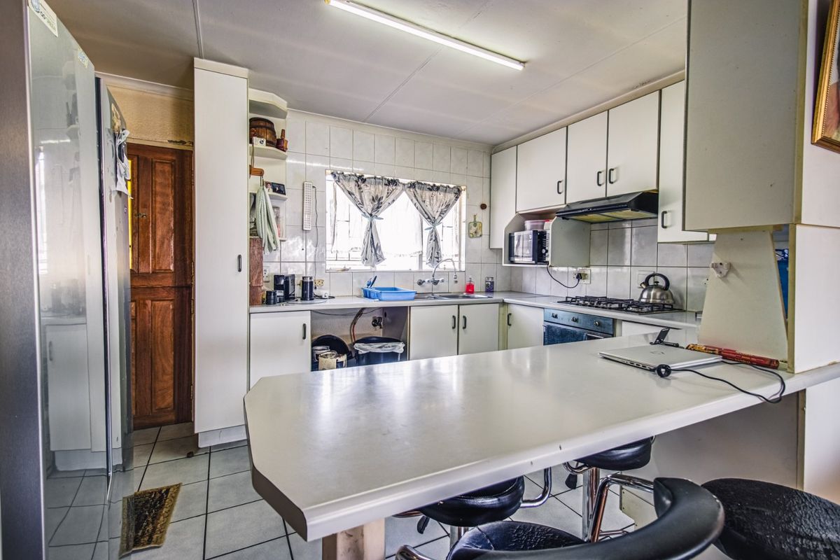 A functional kitchen featuring white cabinetry, a gas hob, built-in oven, and a breakfast bar, offering potential for modernization.