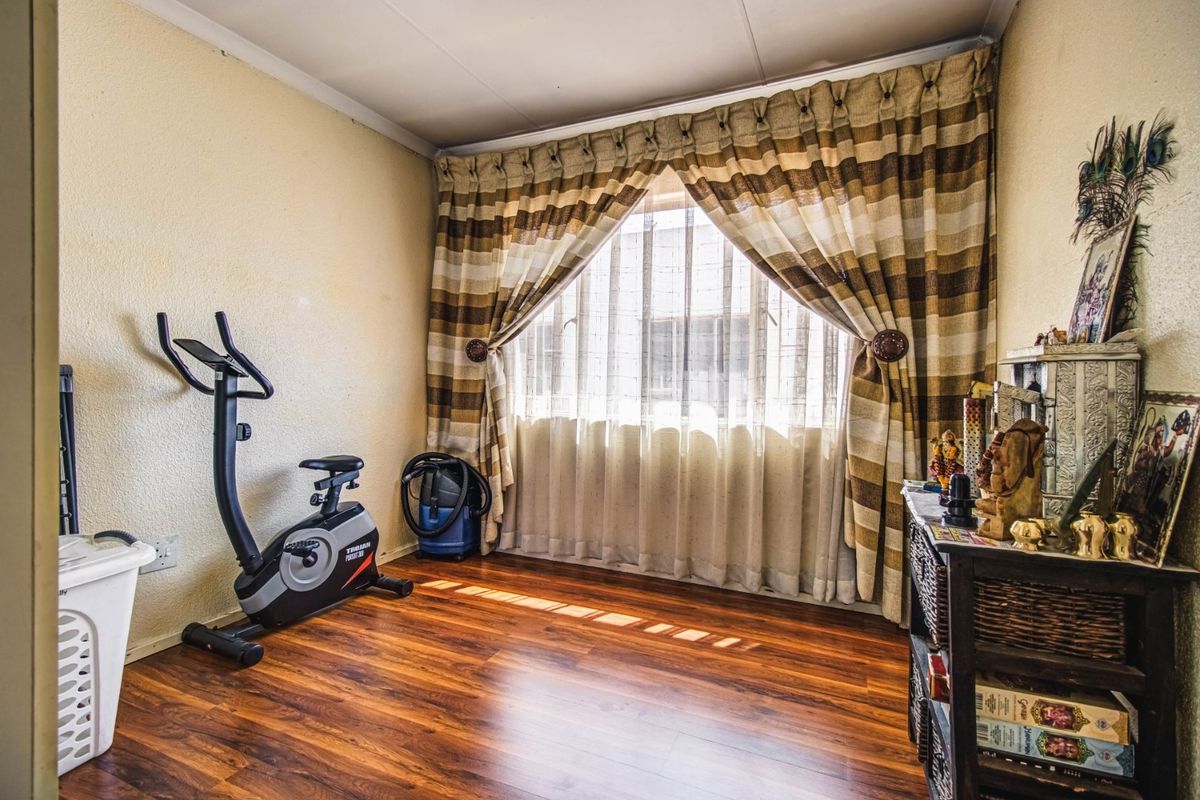 A bedroom featuring laminate flooring and natural light through a window with installed curtain tracks.