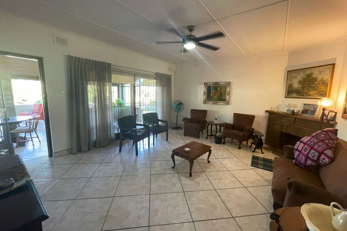 Spacious living room featuring tiled flooring, a brick fireplace, and a ceiling fan, with direct access to an outdoor patio area.