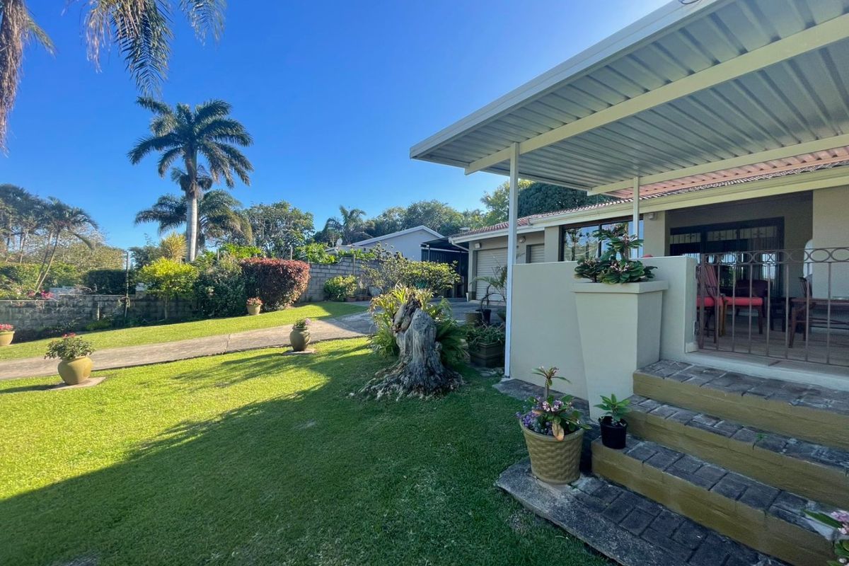 A well-maintained rear exterior view featuring a covered patio, concrete steps, and a spacious landscaped garden with a paved driveway.