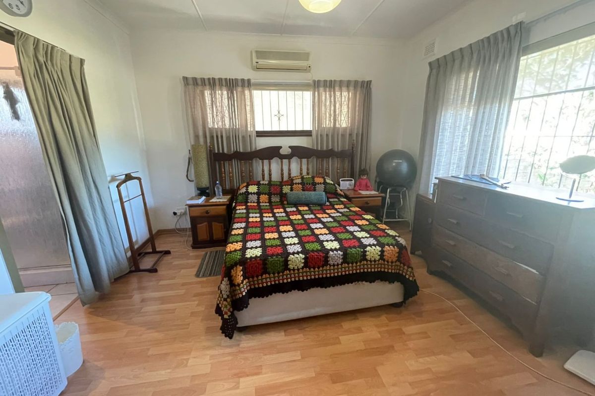 A functional bedroom featuring laminate flooring, a wall-mounted split-system air conditioner, and windows fitted with security bars.