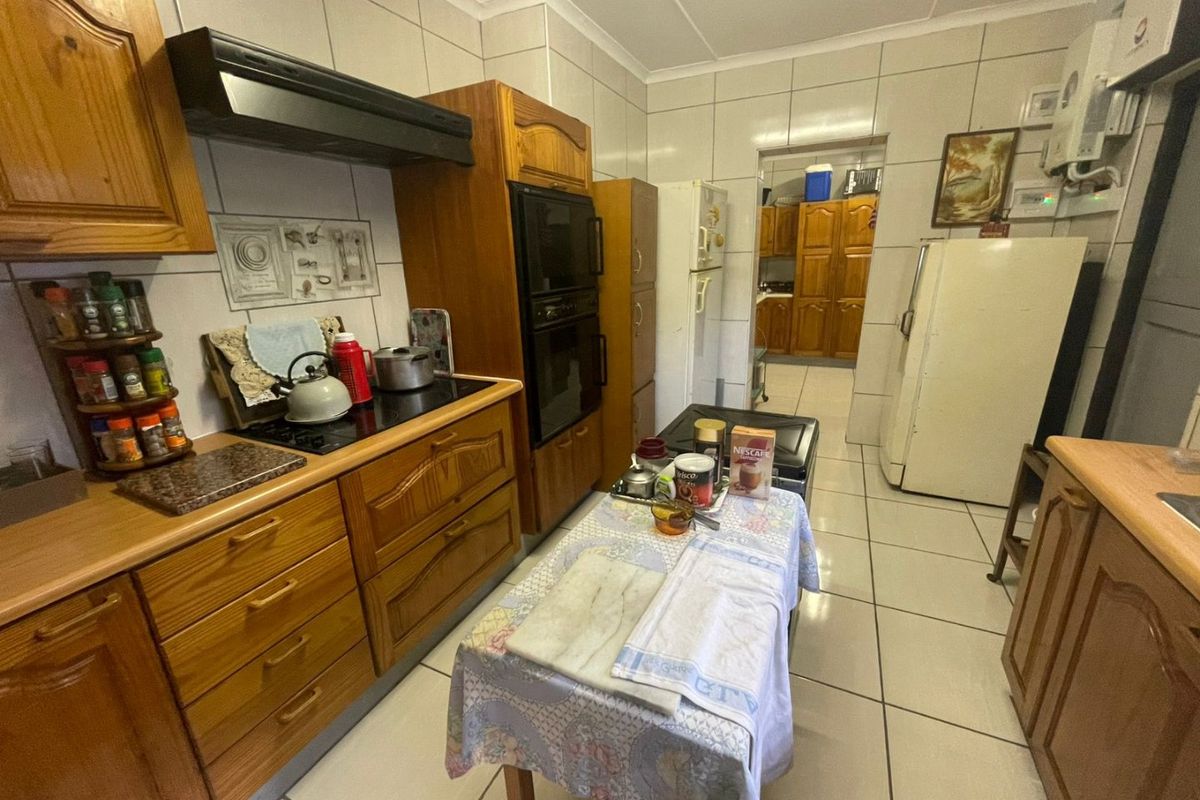 A functional kitchen featuring traditional wooden cabinetry, built-in oven, extractor fan, and tiled finishes, with an adjacent scullery area visible.