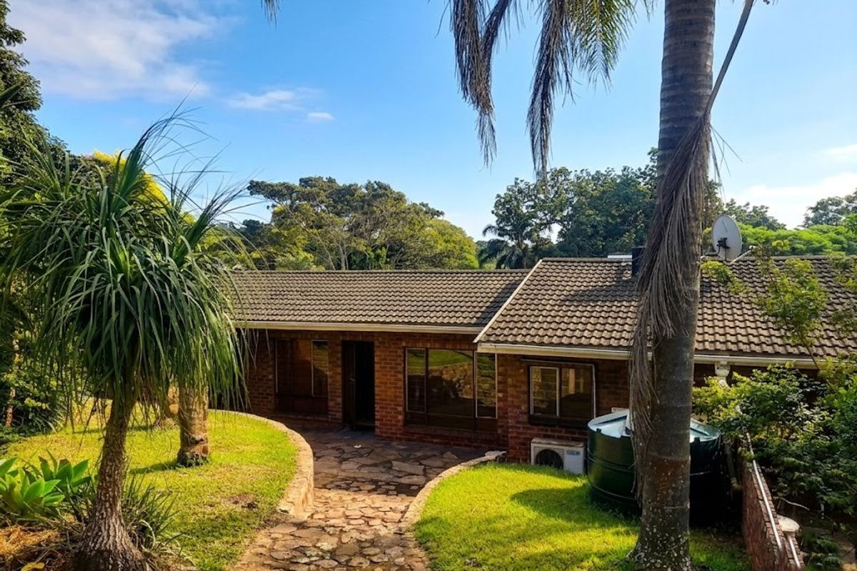 Rear view of a brick house featuring a stone paved pathway, landscaped garden, water storage tank, and tiled roof.