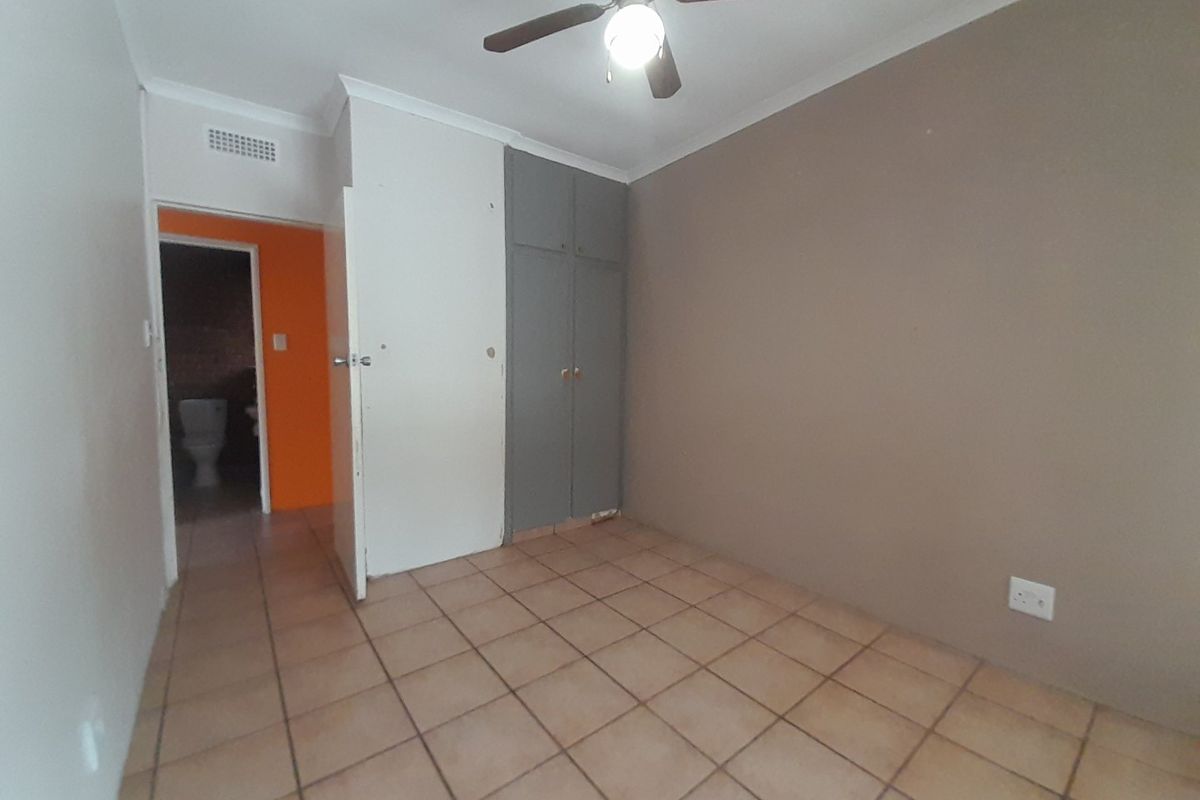 An empty bedroom featuring tiled flooring, a ceiling fan, and built-in cupboards, with an adjacent view into a bathroom area.