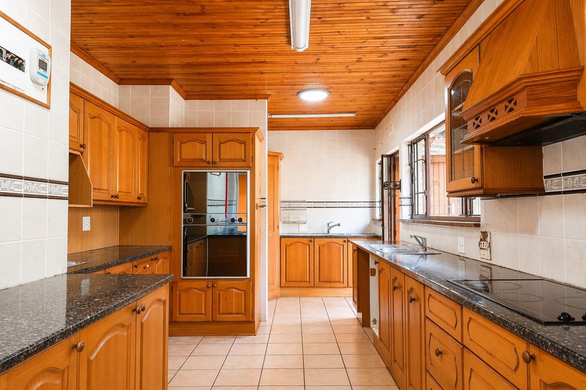 A spacious kitchen featuring traditional wooden cabinetry, granite countertops, built-in appliances, and a warm wooden ceiling, offering a functional layout with ample storage.