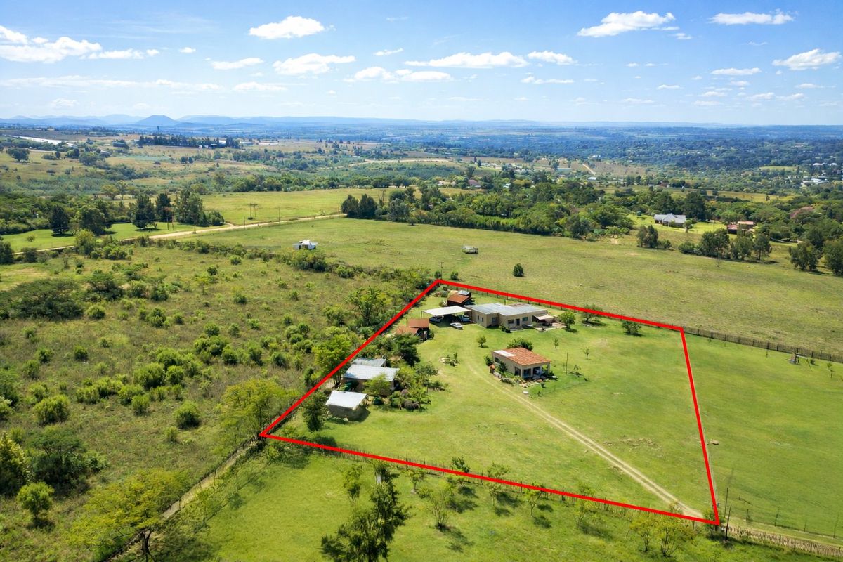 Aerial view of a farm property featuring multiple outbuildings, expansive grounds, and perimeter fencing set within a rural landscape.