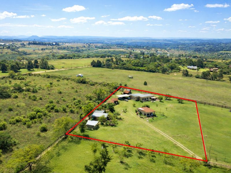 Aerial view of a farm property featuring multiple outbuildings, expansive grounds, and perimeter fencing set within a rural landscape.