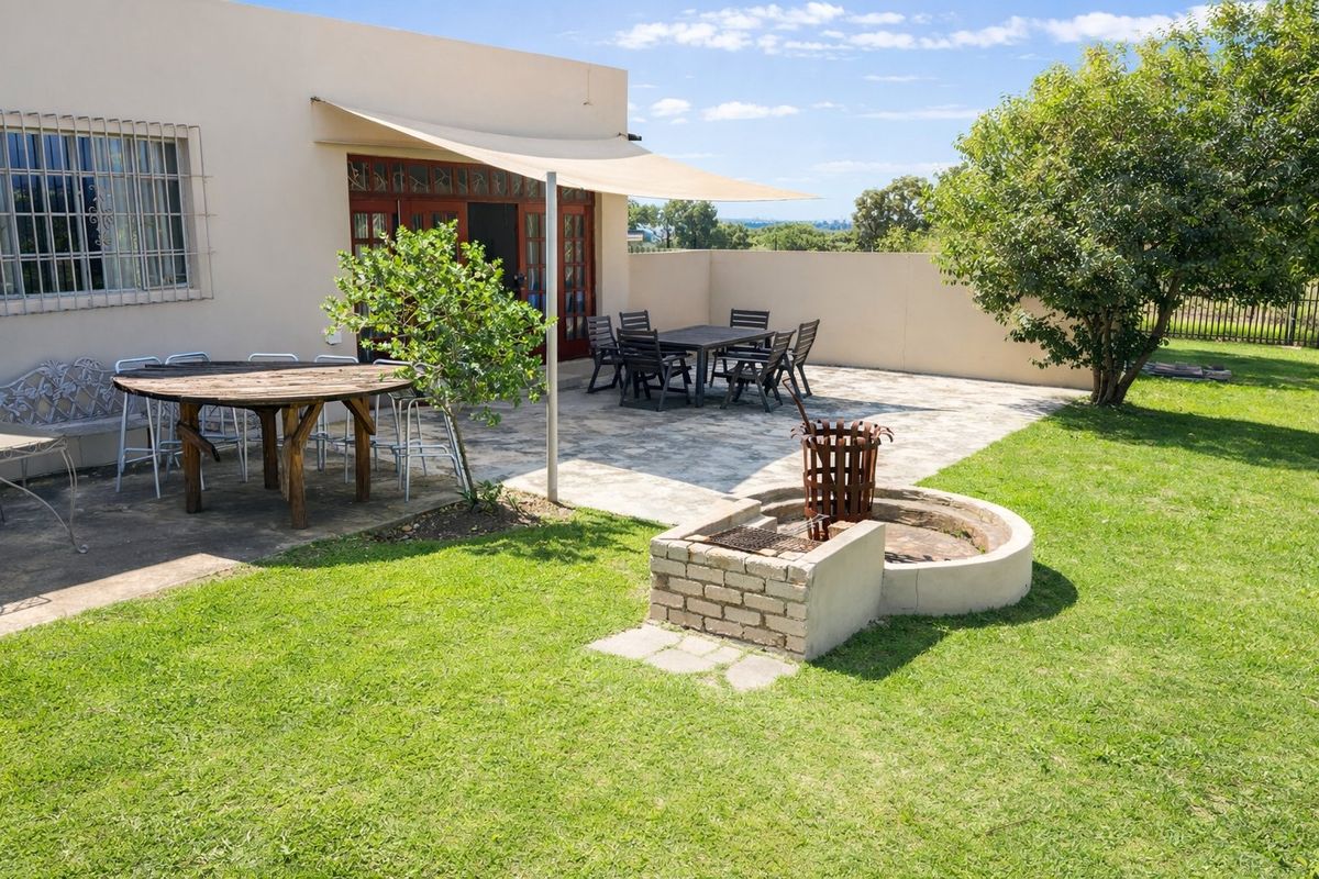 Rear garden area featuring a paved patio, built-in braai, and shade sail, providing a functional outdoor entertainment space.
