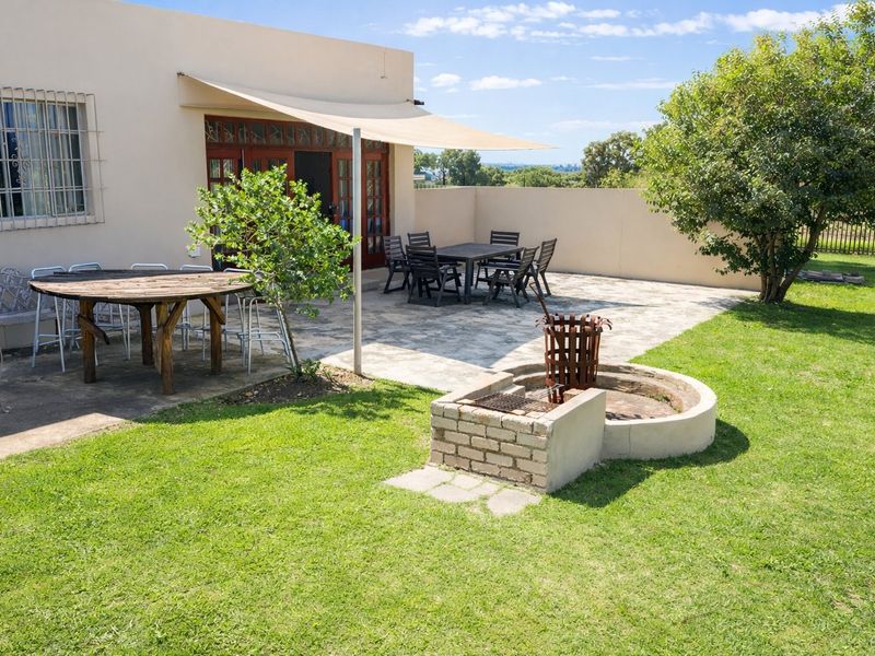 Rear garden area featuring a paved patio, built-in braai, and shade sail, providing a functional outdoor entertainment space.