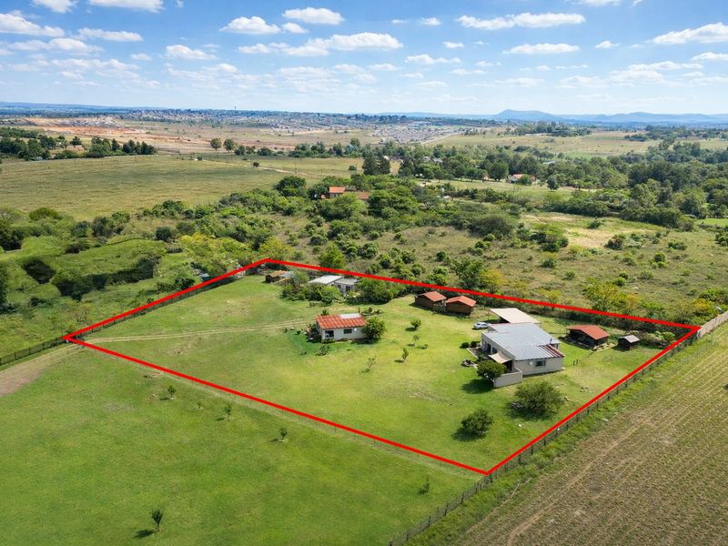 Aerial view of a farm property featuring multiple outbuildings, fenced boundaries, and expansive surrounding landscape.