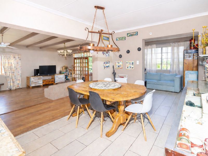 Spacious open-plan living and dining area featuring a mix of tiled and laminate flooring, exposed timber beams, and natural light through security-barred windows.