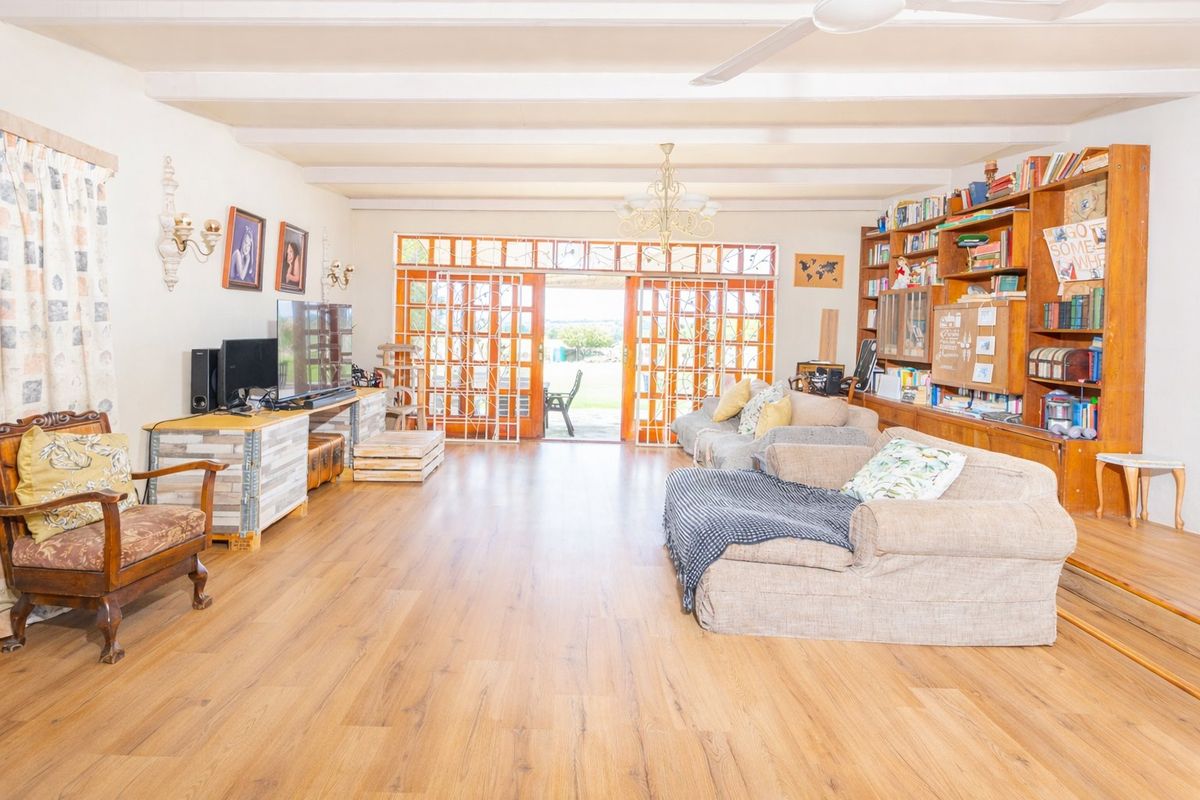 Spacious living room featuring exposed ceiling beams, wood laminate flooring, and a large built-in wooden bookshelf, with direct access to the outdoor patio area.