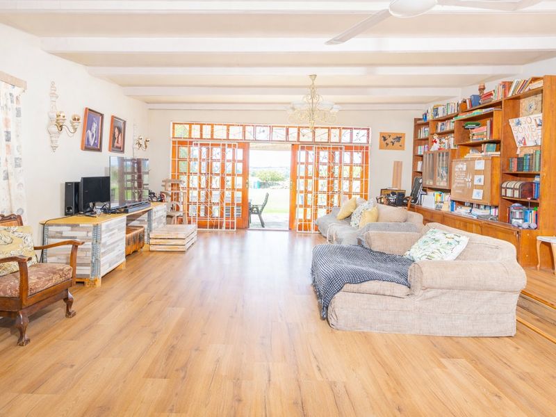 Spacious living room featuring exposed ceiling beams, wood laminate flooring, and a large built-in wooden bookshelf, with direct access to the outdoor patio area.