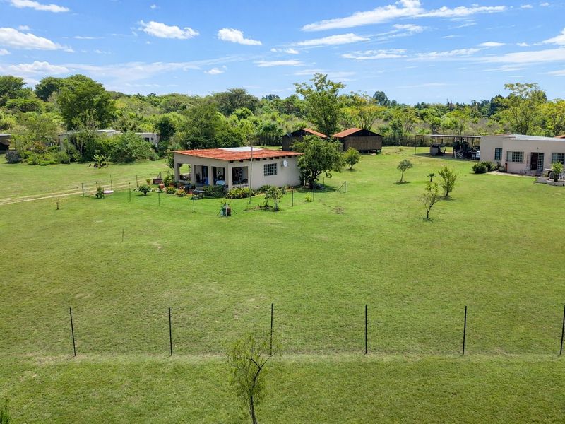 Aerial view of a spacious farm property featuring a main dwelling with a covered patio, multiple outbuildings, and expansive green grounds.