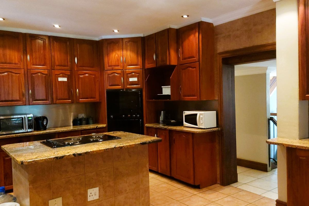 A traditional kitchen featuring warm-toned wooden cabinetry, granite countertops, a central island with a built-in hob, and tiled flooring throughout.