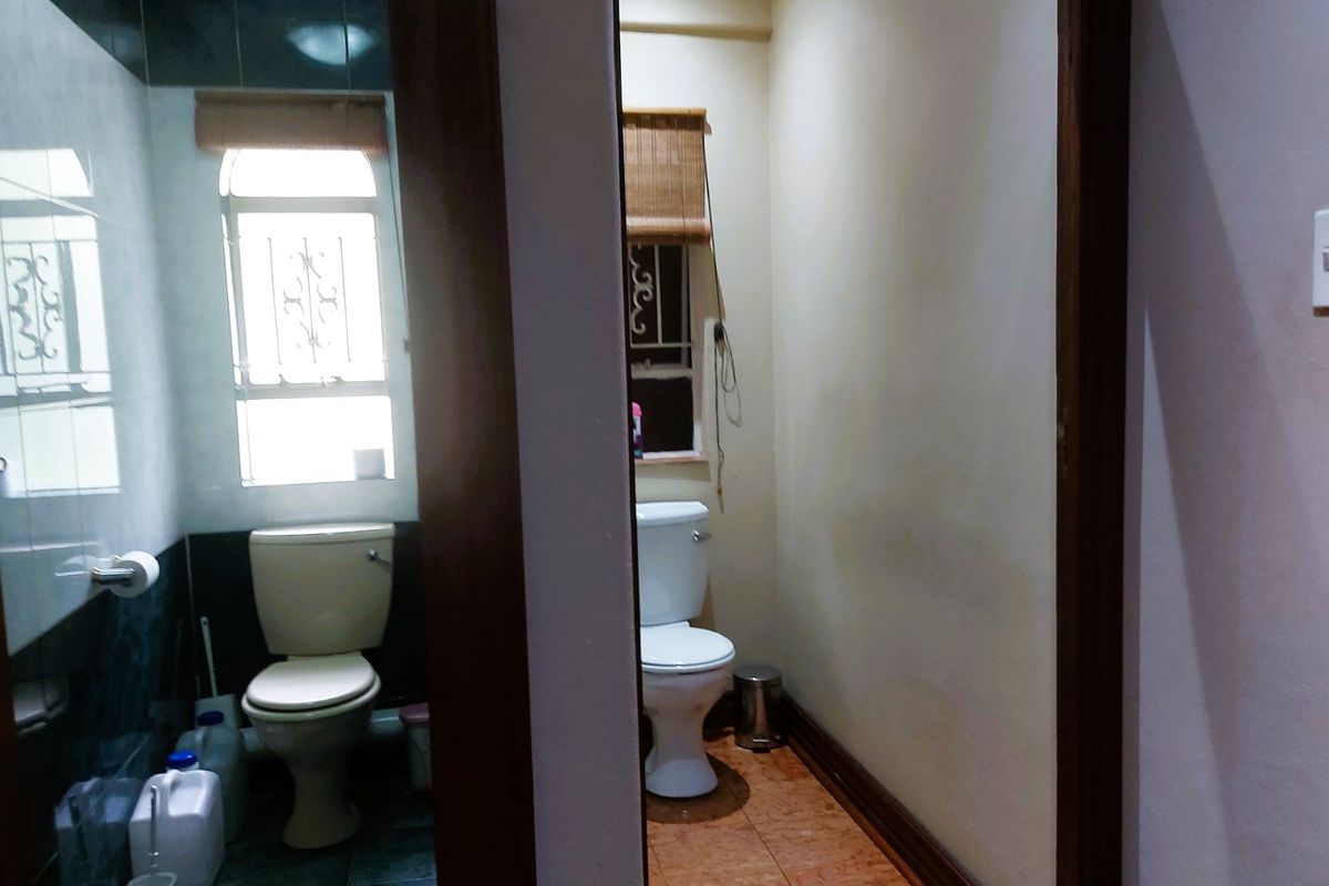 A view of two separate bathroom spaces featuring basic toilets, tiled flooring, and windows with security bars, requiring cosmetic updates.