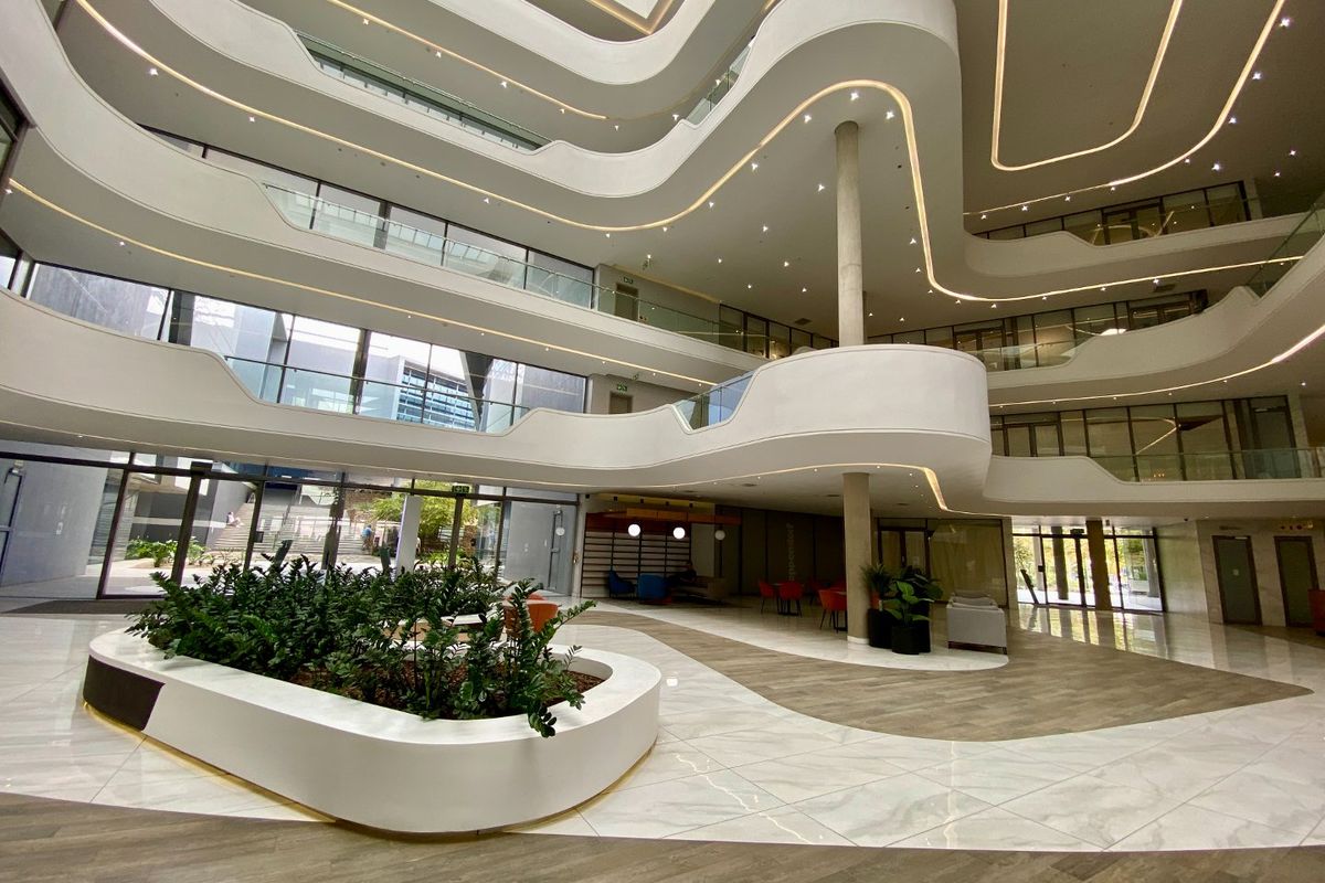 Spacious modern commercial atrium featuring a multi-level mezzanine, glass balustrades, recessed architectural lighting, and high-end marble-look flooring.