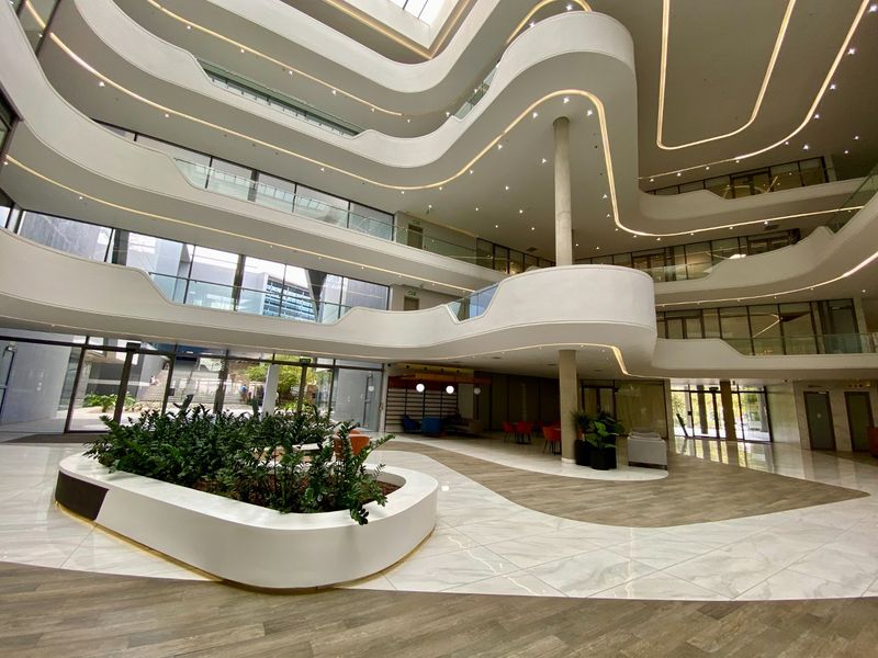 Spacious modern commercial atrium featuring a multi-level mezzanine, glass balustrades, recessed architectural lighting, and high-end marble-look flooring.