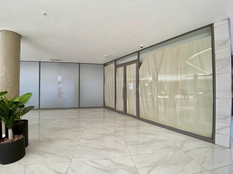 Modern commercial entrance lobby featuring polished marble-look floor tiles, extensive glass partitioning, and a clean, professional aesthetic suitable for a corporate or retail space.
