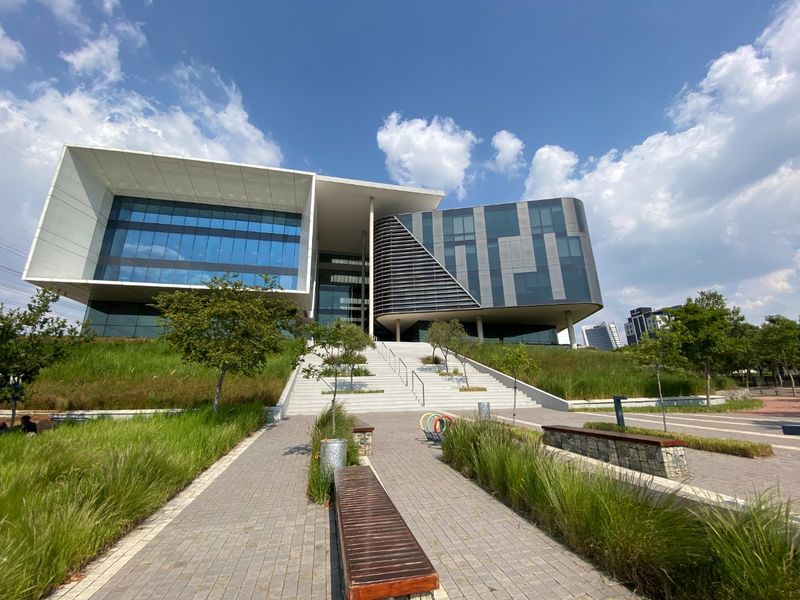 Modern commercial office building featuring a striking glass facade, cantilevered architectural design, and a landscaped approach with wide concrete stairs.
