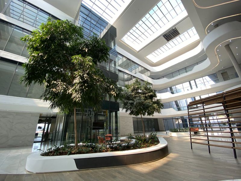 Spacious modern commercial atrium featuring a large glass skylight, marble flooring, and central built-in planters with integrated glass elevator access.