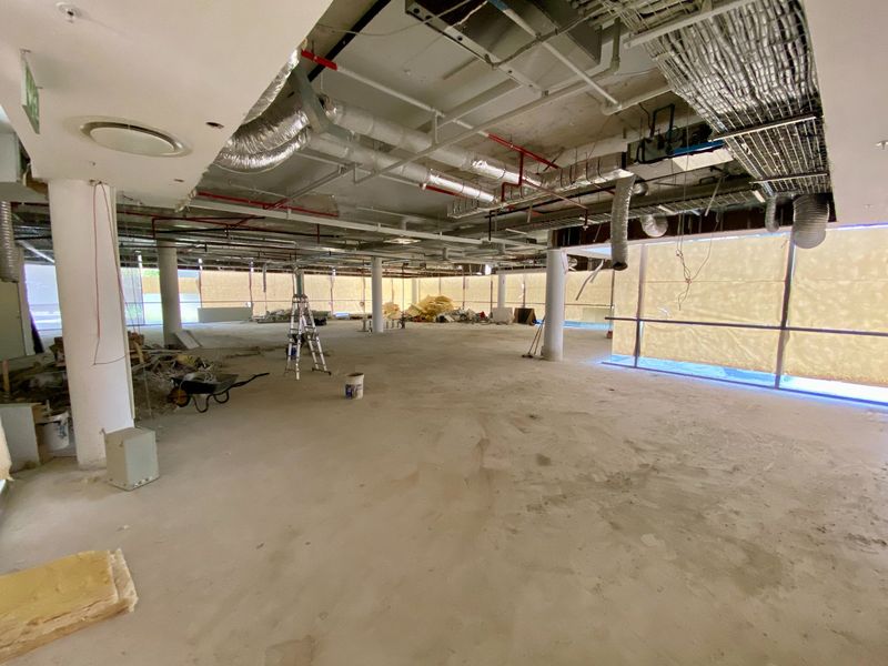A large, open-plan commercial space currently under construction, featuring exposed ceiling services, structural columns, and expansive floor-to-ceiling windows.