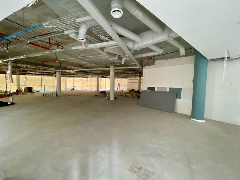 A large, open-plan commercial space currently under construction, featuring exposed industrial ceilings, structural columns, and unfinished concrete flooring.