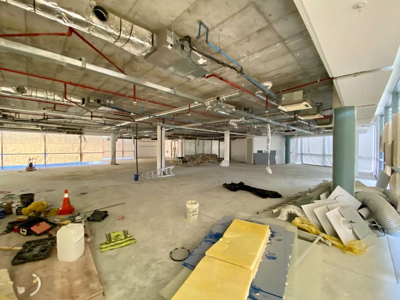 An expansive, unfinished open-plan commercial space featuring exposed industrial ceilings, structural columns, and large windows, currently undergoing construction or renovation.