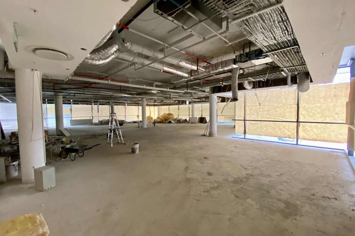 Large open-plan commercial space currently under renovation, featuring exposed industrial ceilings, concrete columns, and expansive floor-to-ceiling windows.