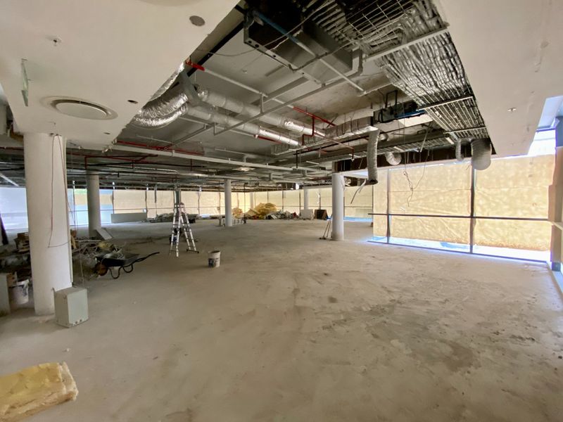 Large open-plan commercial space currently under renovation, featuring exposed industrial ceilings, concrete columns, and expansive floor-to-ceiling windows.
