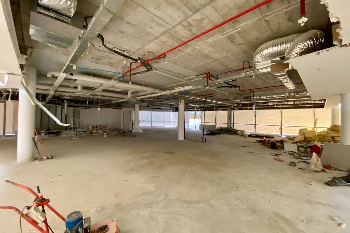 Large open-plan commercial space currently under construction, featuring exposed industrial ceilings, structural columns, and expansive windows awaiting final fit-out.