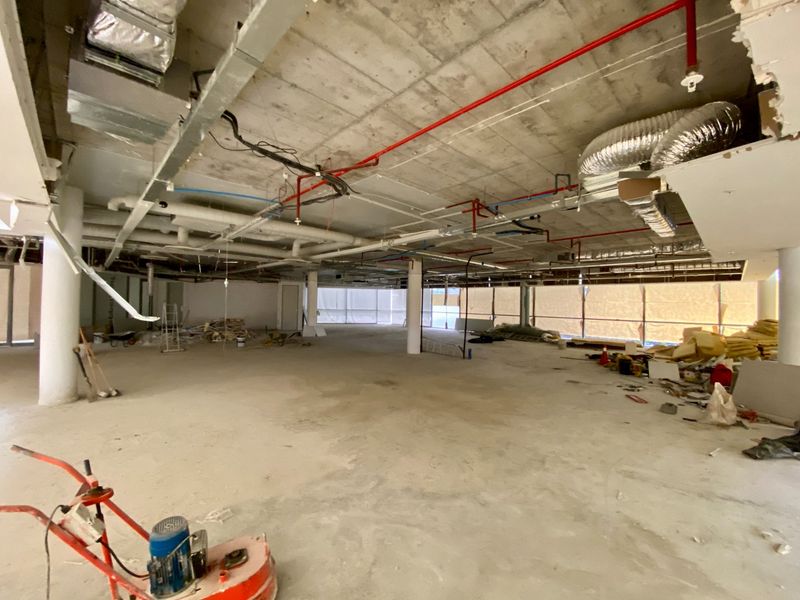 Large open-plan commercial space currently under construction, featuring exposed industrial ceilings, structural columns, and expansive windows awaiting final fit-out.