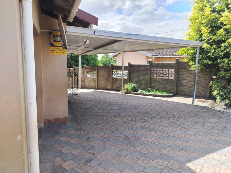 A paved driveway area featuring a covered carport and secure brick boundary walling.