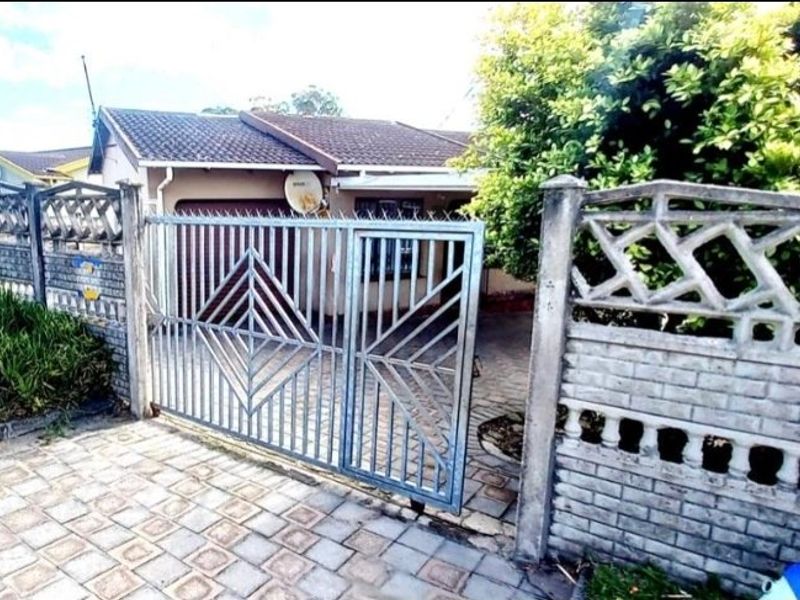 Front view of the property featuring a paved driveway, metal security gate, and precast concrete boundary wall.