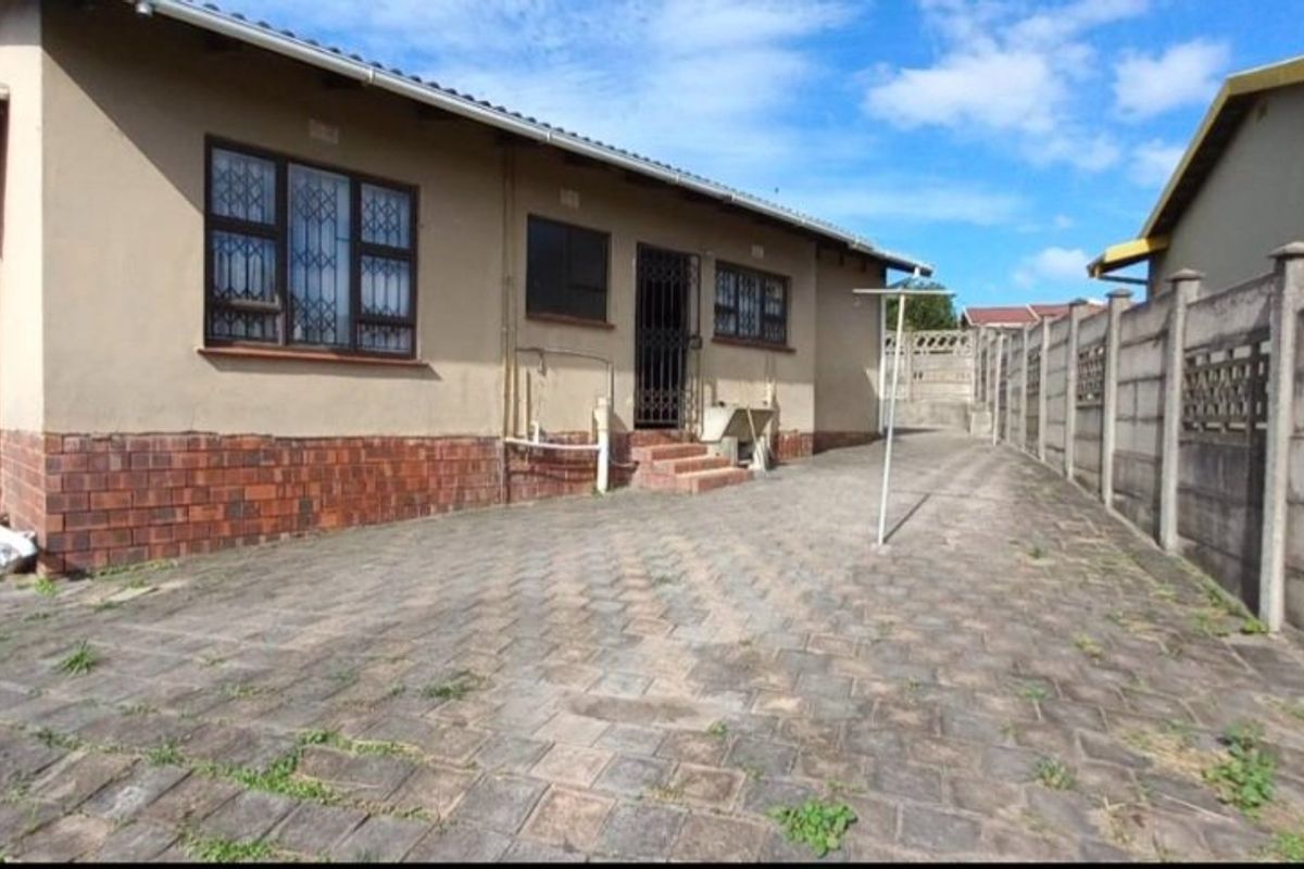 Rear exterior view of the house featuring paved driveway area, precast concrete boundary walls, and security bars on windows.