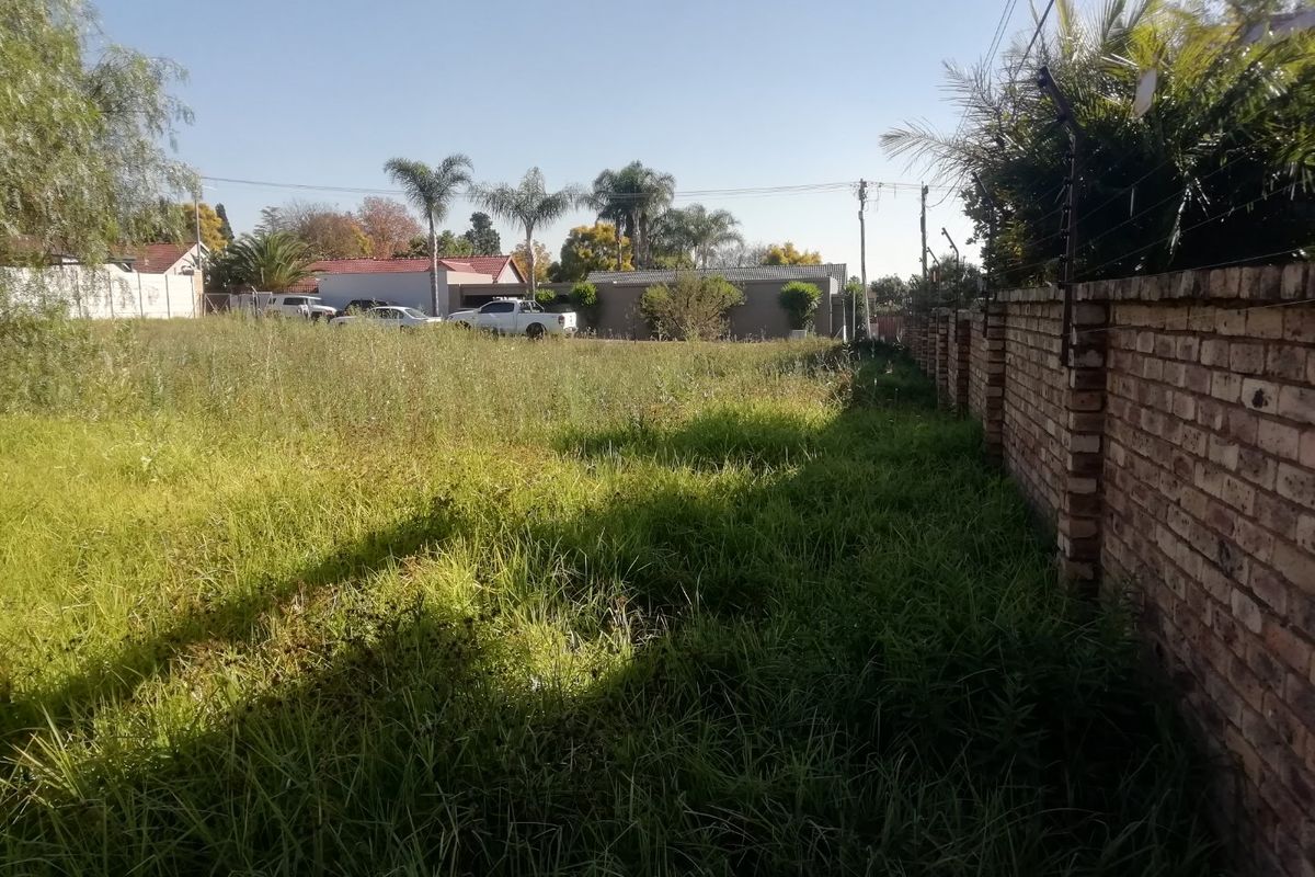 A vacant residential plot featuring an established brick boundary wall with electric fencing, currently covered in overgrown grass and vegetation.