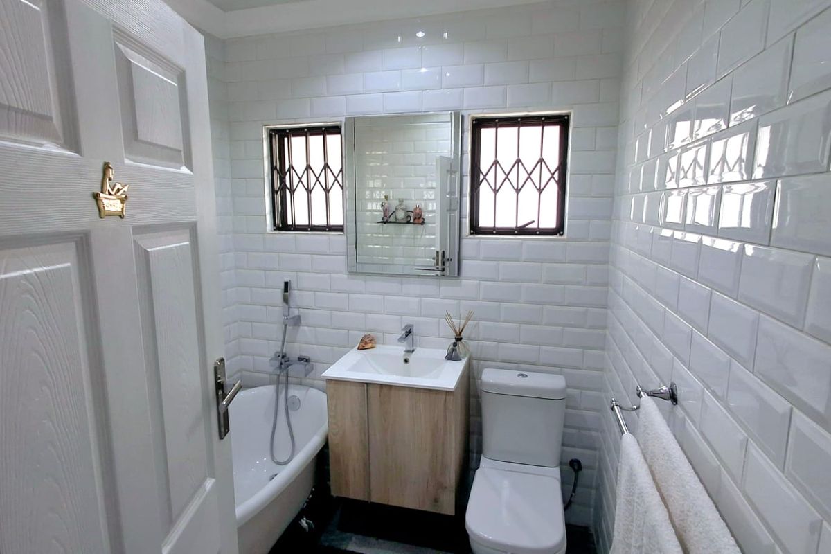 A modern bathroom featuring white subway wall tiles, a vanity cabinet with a basin, a bathtub with a handheld shower, and a toilet.