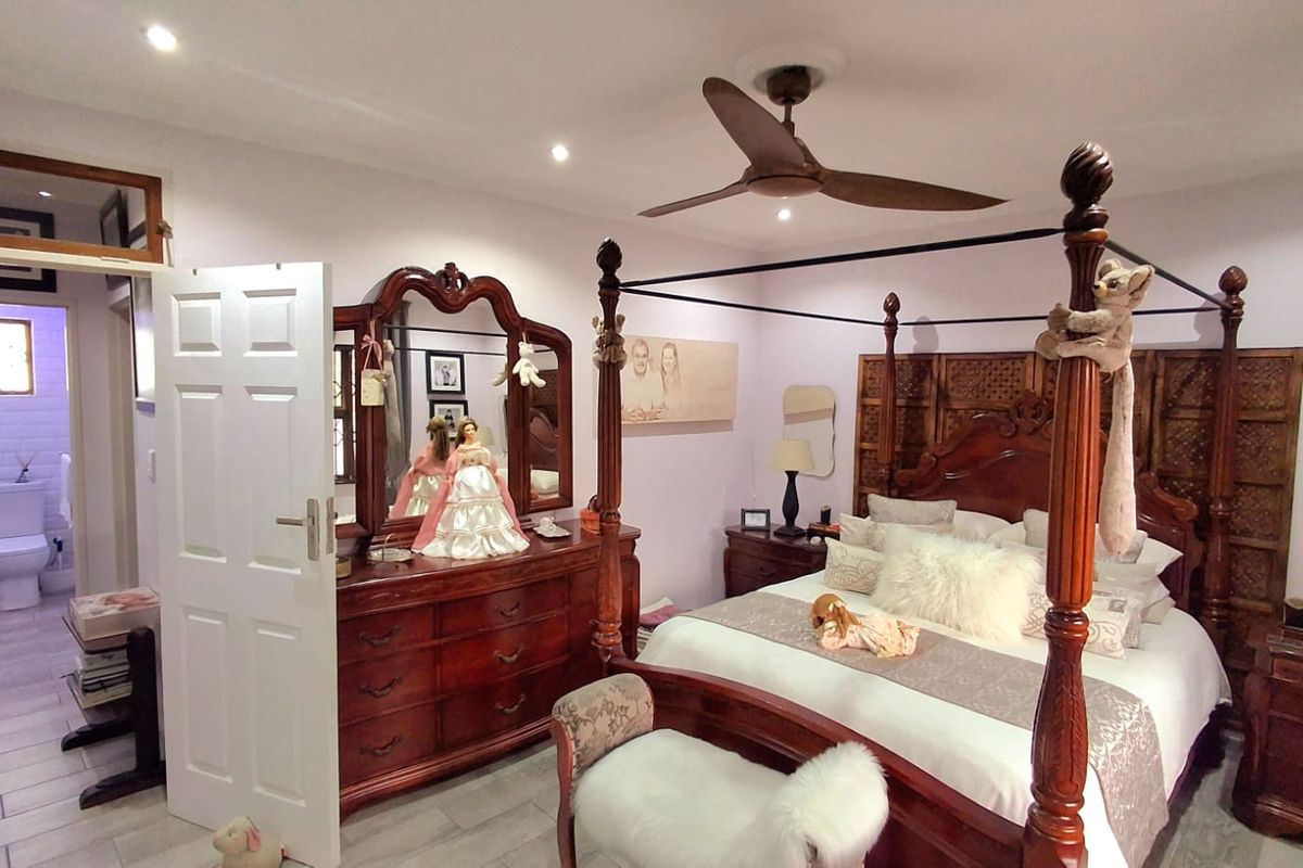 Spacious bedroom featuring a four-poster bed, ceiling fan, and recessed lighting, with an adjoining en-suite bathroom visible through the doorway.