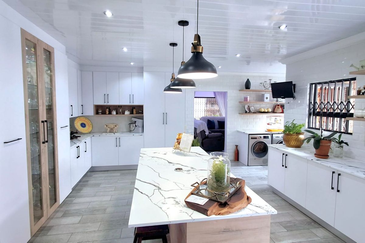 Modern open-plan kitchen featuring a large marble-topped island, sleek white cabinetry, integrated appliances, and contemporary pendant lighting.