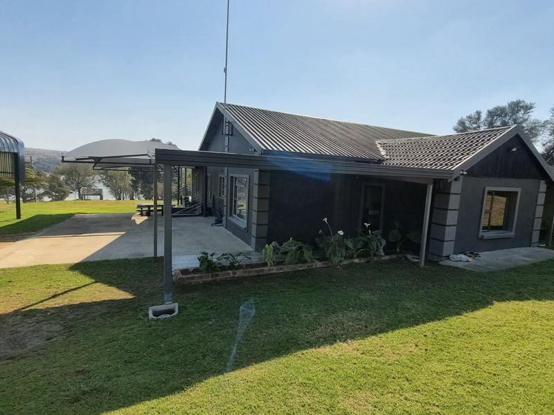 Rear view of the house featuring a covered patio area, concrete flooring, and a metal roof, set within a spacious garden.