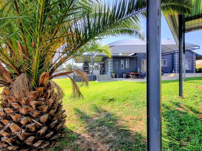 A spacious rear garden featuring a covered patio area with a built-in braai, shade sail, and well-maintained lawn.