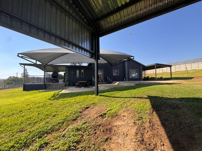 Rear exterior view featuring a large shade sail over a concrete patio, built-in braai area, and expansive lawn space.