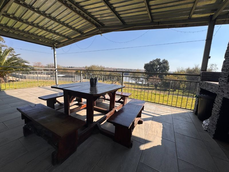 Covered outdoor patio featuring tiled flooring, a built-in stone-clad braai, and metal railing, offering scenic views of the surrounding landscape.