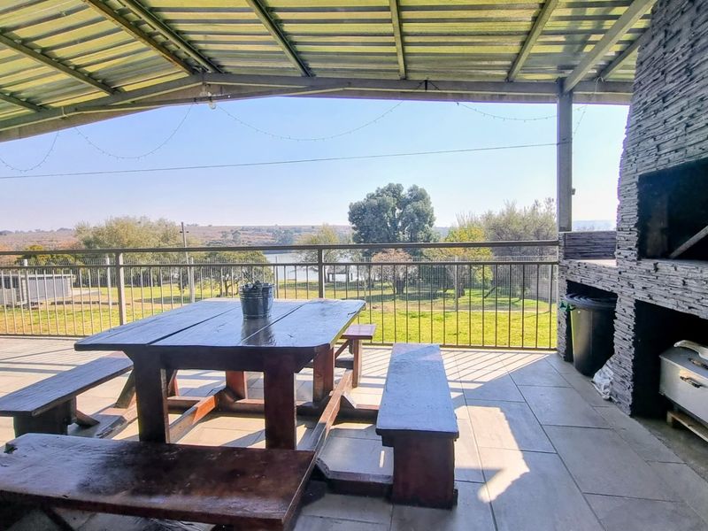 Covered outdoor patio featuring a built-in stone-clad braai, tiled flooring, and expansive views of the surrounding landscape.
