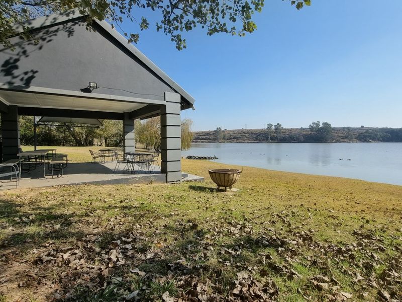 A covered outdoor patio area featuring concrete pillars and flooring, overlooking a scenic lakefront setting.