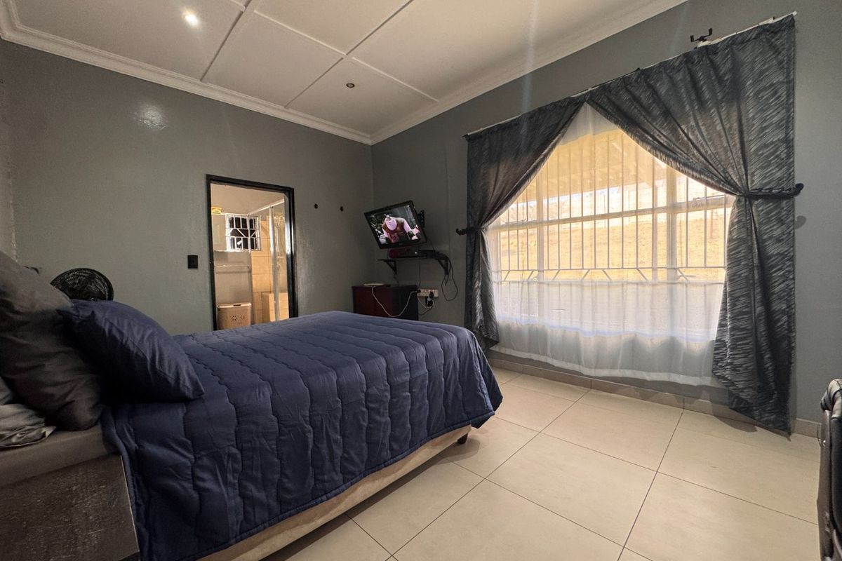 A bedroom featuring tiled flooring, security bars on the window, and direct access to an en-suite bathroom.