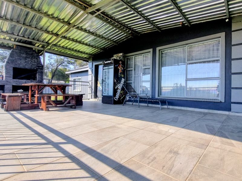 A spacious covered patio featuring a built-in stone braai, tiled flooring, and direct access to the home through large sliding glass doors.