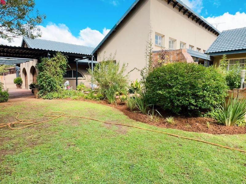 A well-maintained rear exterior view featuring a landscaped garden, paved patio area, and covered walkway connecting the building sections.