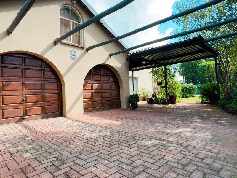 Front exterior view featuring a double garage with arched wooden doors, a brick-paved driveway, and a covered carport area.
